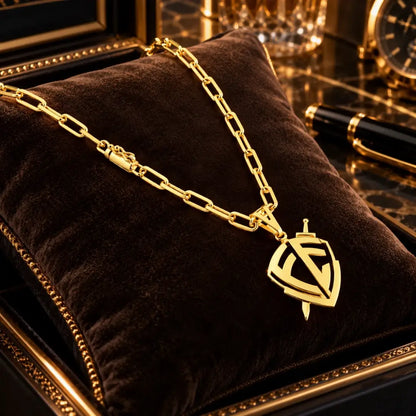 Colar masculino banhado a ouro 18k com corrente Cartier e pingente escudo de fé vazado com espada apoiado sobre almofada de veludo preto.