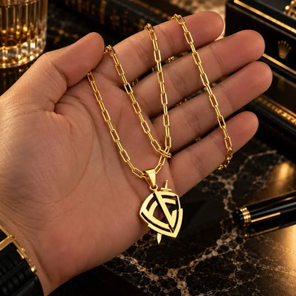Mão masculina segurando o colar banhado a ouro 18k com corrente Cartier e pingente escudo de fé para visualização de escala e proporção.
