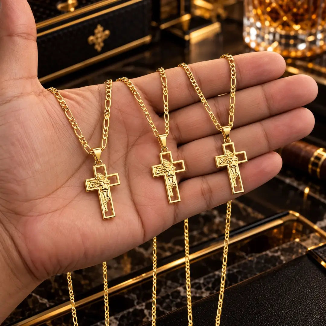 Mão masculina segurando três colares banhados a ouro 18k com corrente 3x1 e pingente de cruz com a face de Jesus Cristo para comparação de tamanho.
