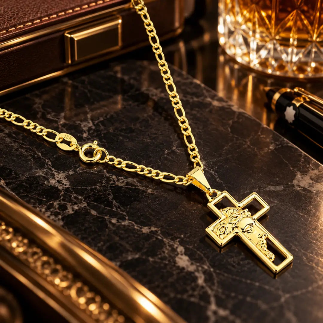 Pingente de cruz vazada com a face de Jesus Cristo em alto relevo ao lado do fecho e da corrente 3x1 banhada a ouro 18k em bancada luxuosa.