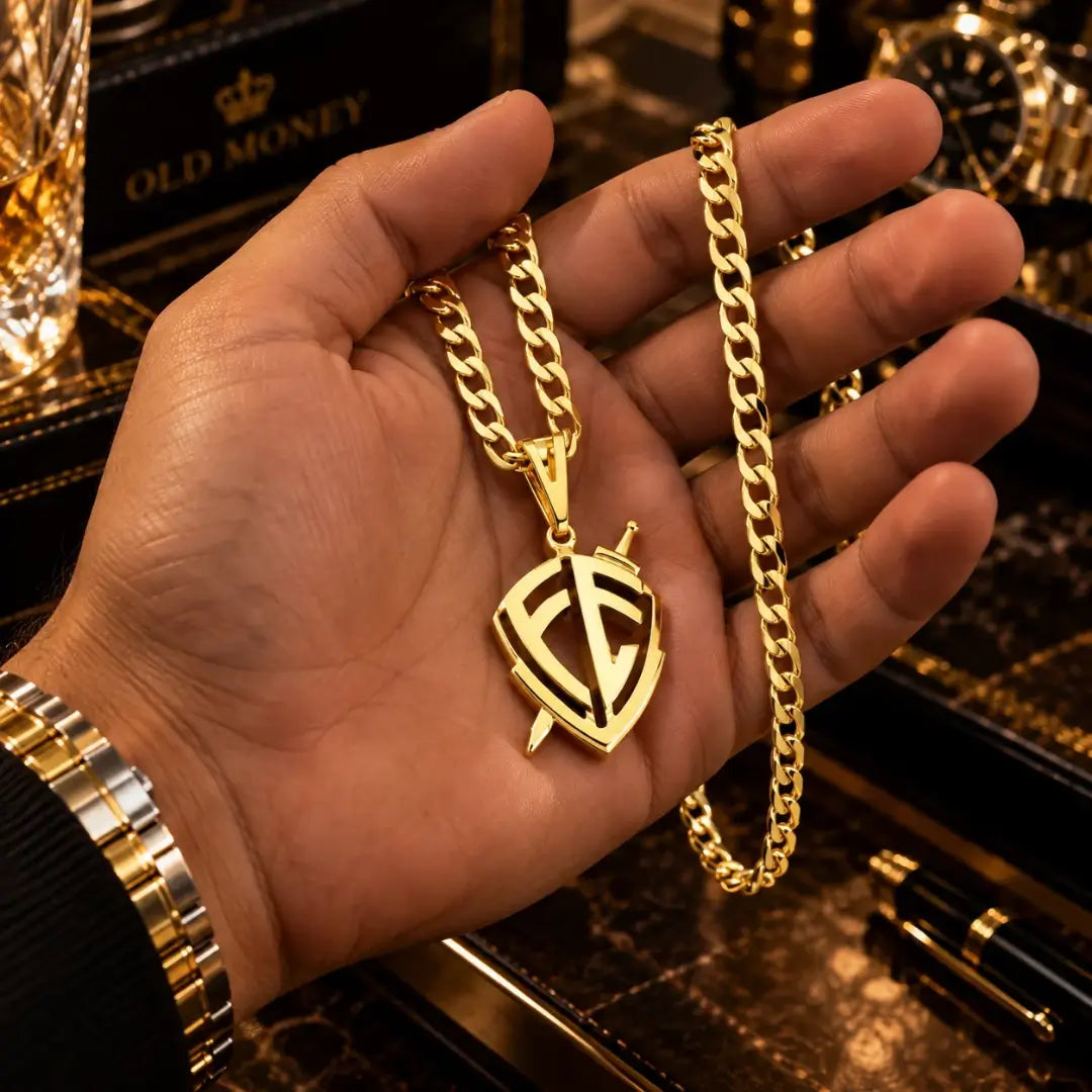 Mão masculina segurando a corrente Grumet banhada a ouro 18k com o pingente Escudo da Fé para demonstração de proporção e tamanho.