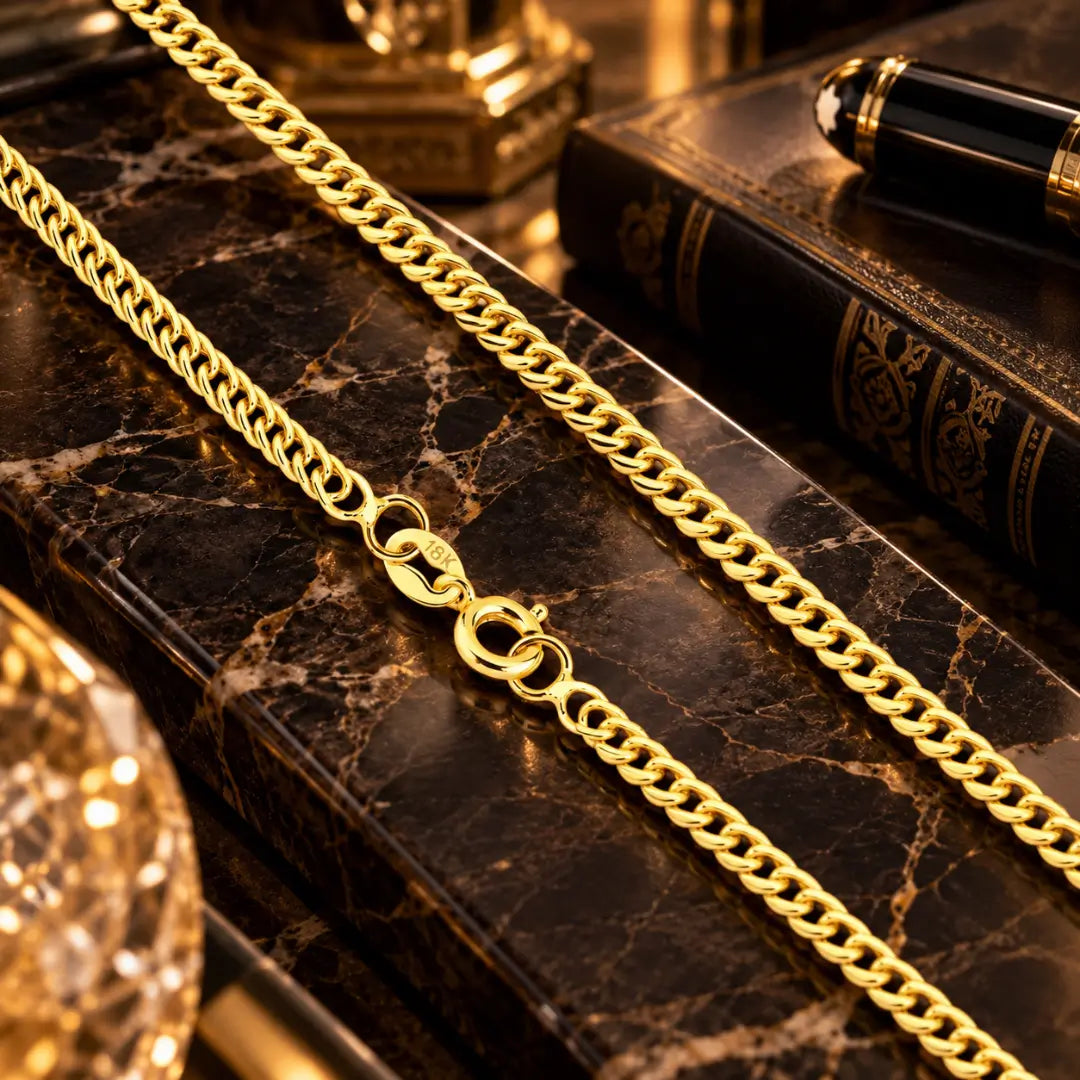 Detalhe em aproximação da corrente grumet dupla banhada a ouro 18k destacando o fecho boia com gravação de autenticidade 18K sobre bancada de mármore escura.