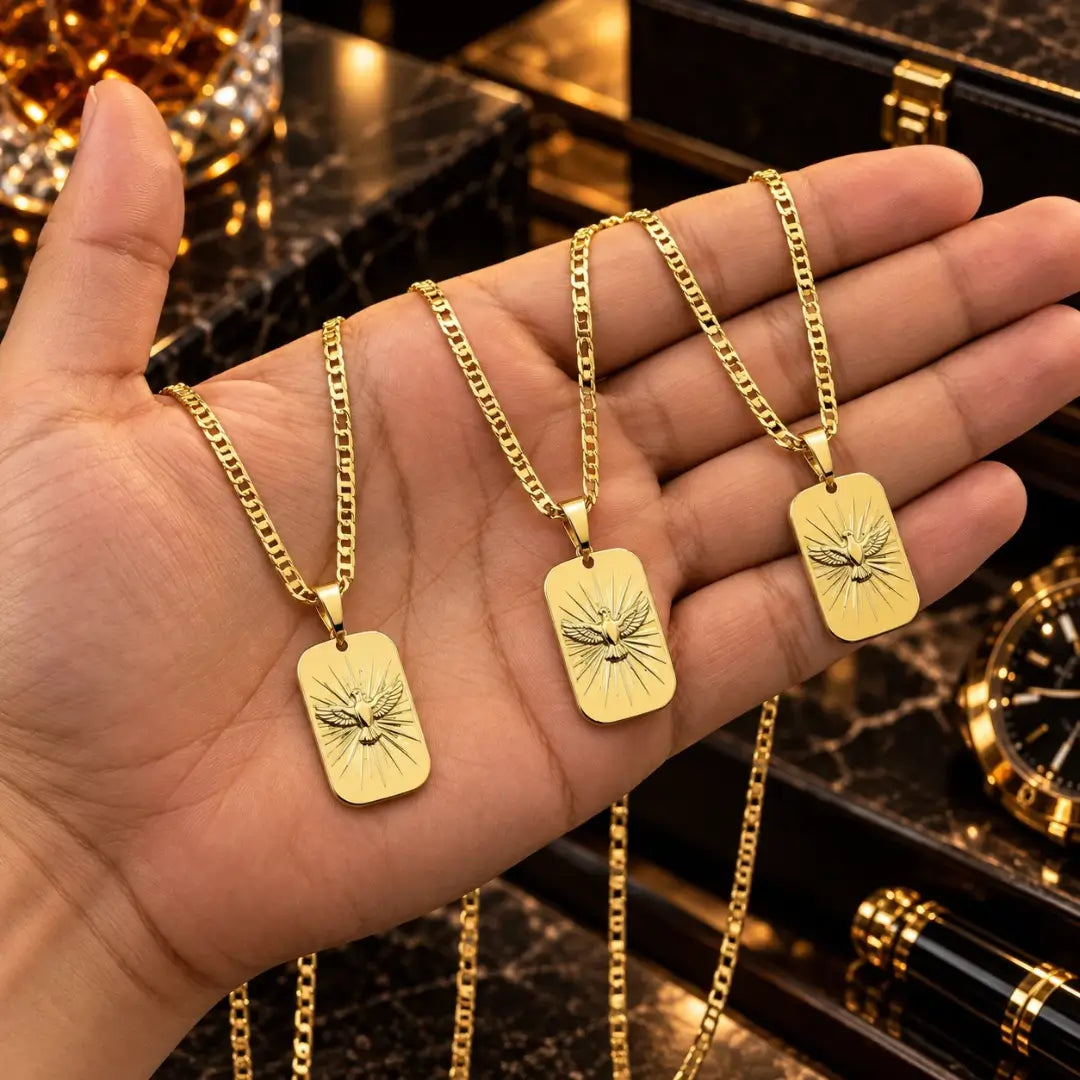 Mão masculina segurando três colares banhados a ouro 18k com corrente piastrini e pingente medalha do Espírito Santo para comparação de tamanho.