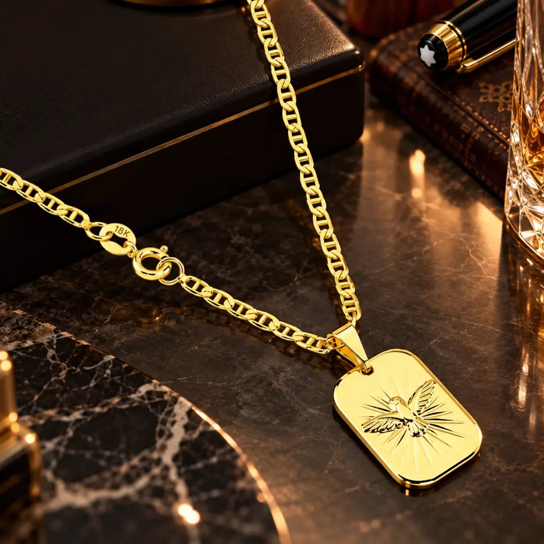 Pingente medalha retangular com a pomba do Espírito Santo e raios gravados em relevo ao lado da corrente piastrini banhada a ouro 18k.