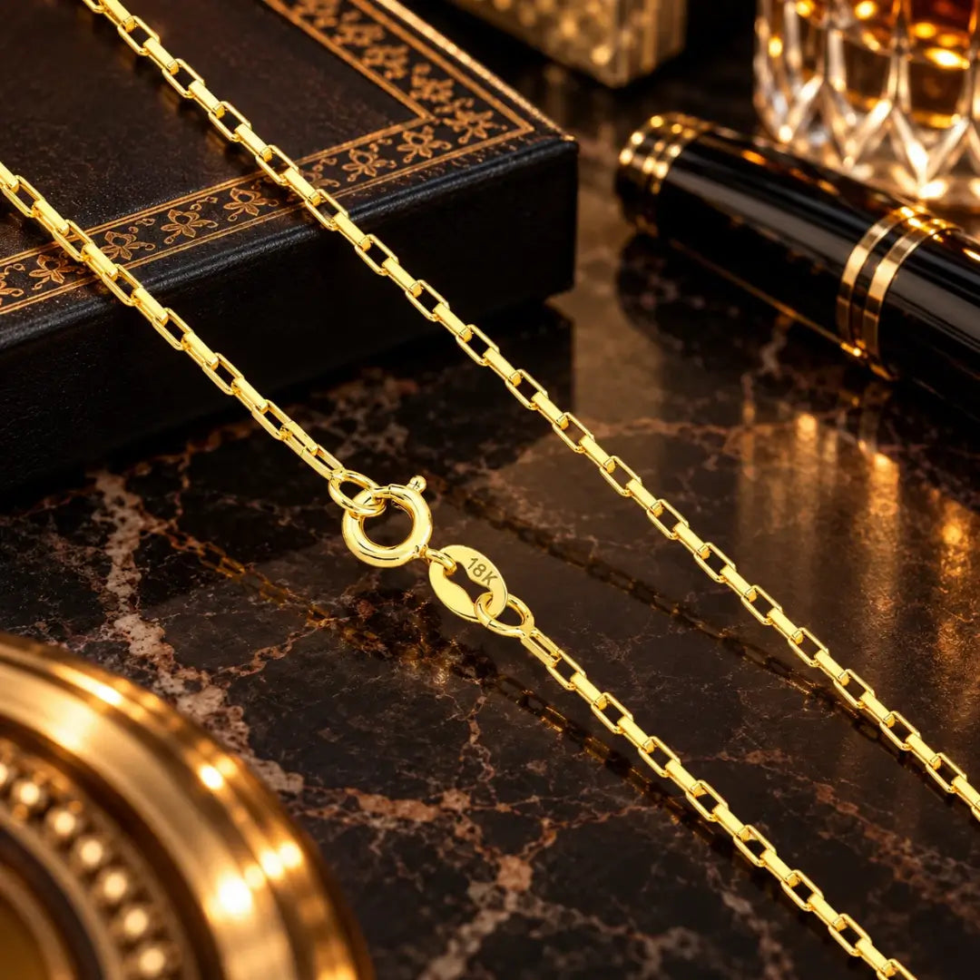 Detalhe da corrente estilo tijolinho banhada a ouro 18k mostrando o fecho boia com gravação da marcação de autenticidade 18K sobre superfície de mármore.