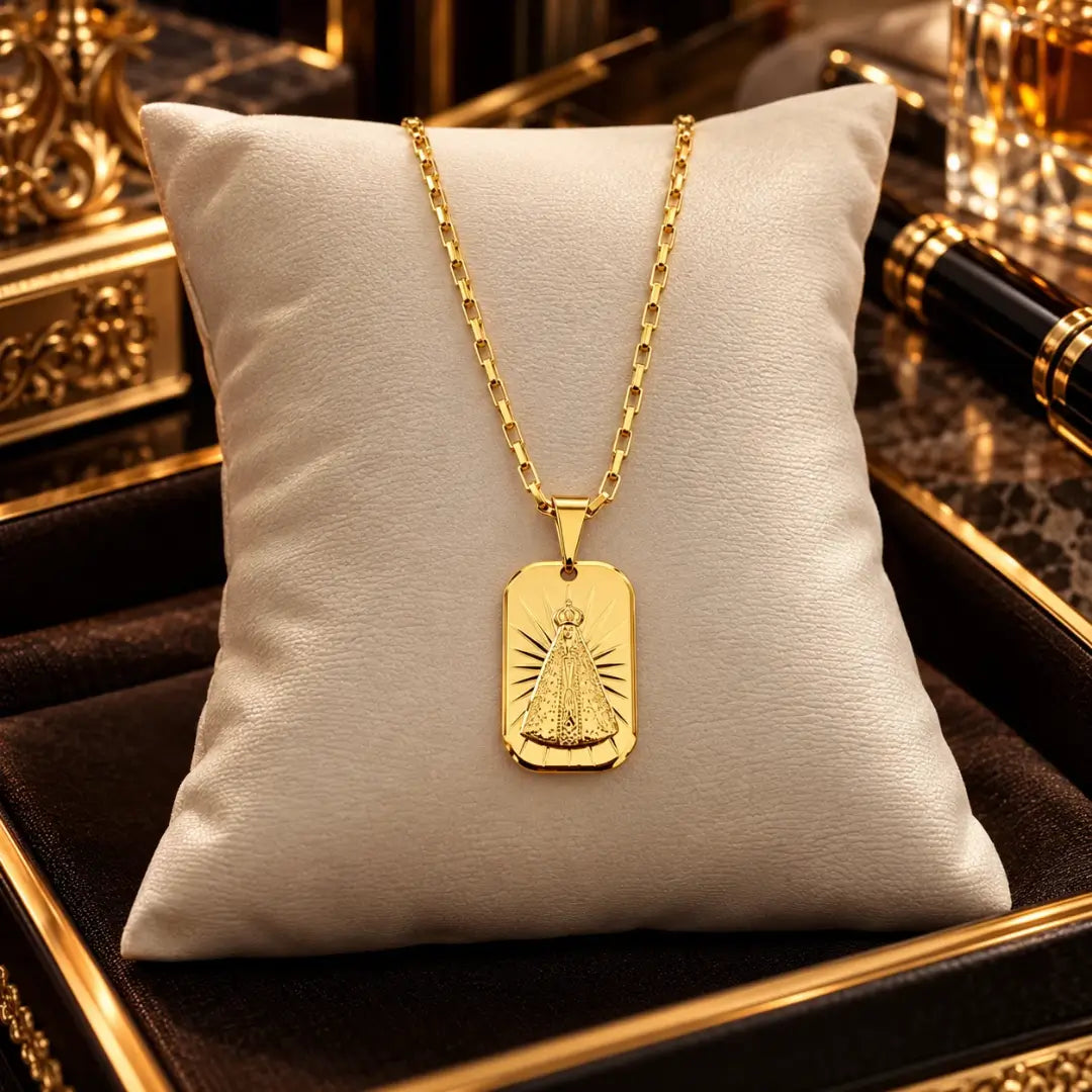 Colar masculino com corrente tijolinho e pingente medalha de Nossa Senhora banhados a ouro 18k acomodados sobre uma almofada clara de veludo.