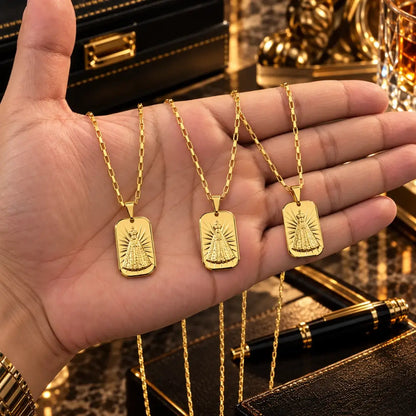 Mão masculina segurando três colares banhados a ouro 18k com corrente tijolinho e pingente de Nossa Senhora Aparecida para visualização de proporção.