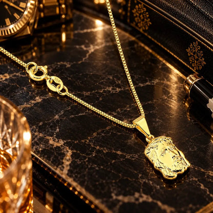 Visão superior da corrente veneziana banhada a ouro 18k com fecho boia gravado 18K e pingente grande da Face de Cristo sobre bancada de mármore escura.