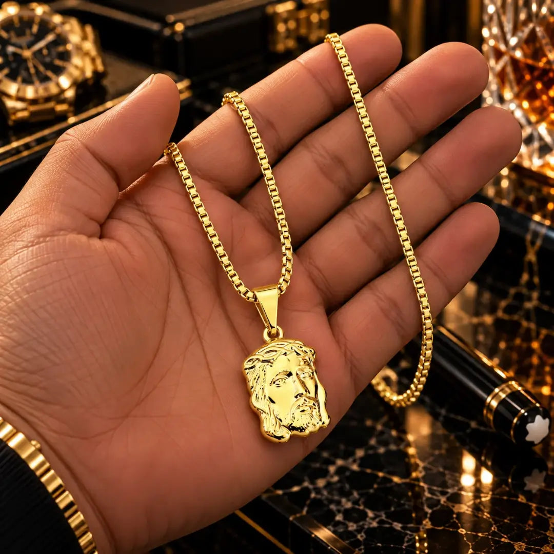 Mão masculina segurando o colar banhado a ouro 18k com corrente veneziana e o pingente grande da Face de Cristo para demonstração de tamanho.