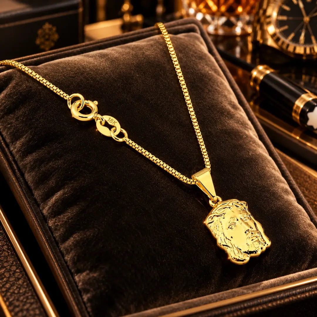 Colar masculino banhado a ouro 18k com corrente veneziana, fecho boia e pingente da Face de Cristo dispostos sobre almofada de veludo marrom.