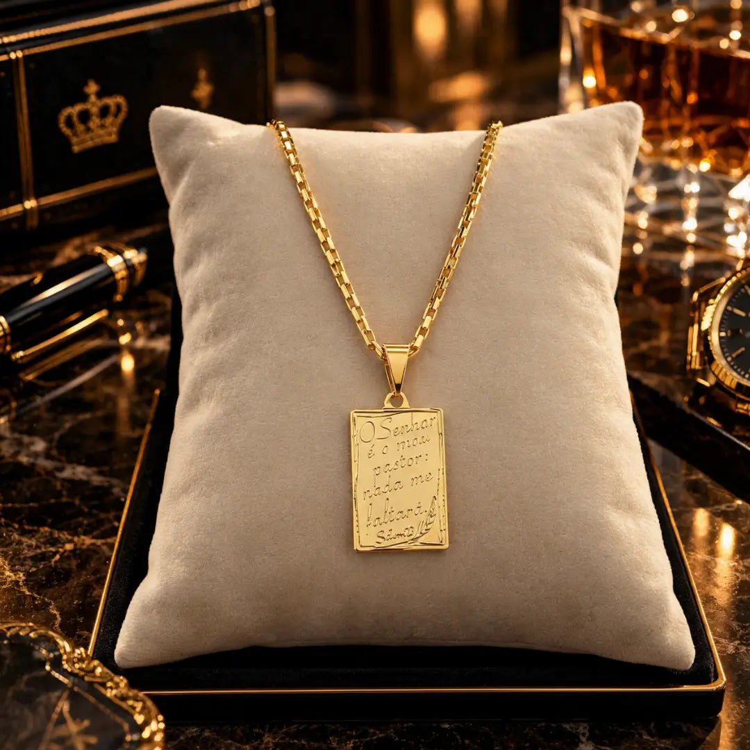 Colar masculino Salmos 23 banhado a ouro 18K com pingente de plaquinha religiosa exposto sobre almofada bege.