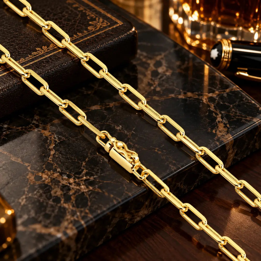 Detalhe em aproximação da corrente estilo Cartier banhada a ouro 18k com espessura de 4.5mm destacando o fecho canhão reforçado sobre mármore.